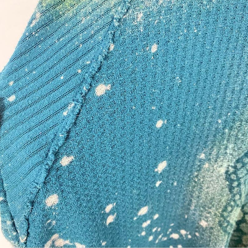 May include: Teal waffle knit fabric with white bleach splatters. The fabric has a textured surface.