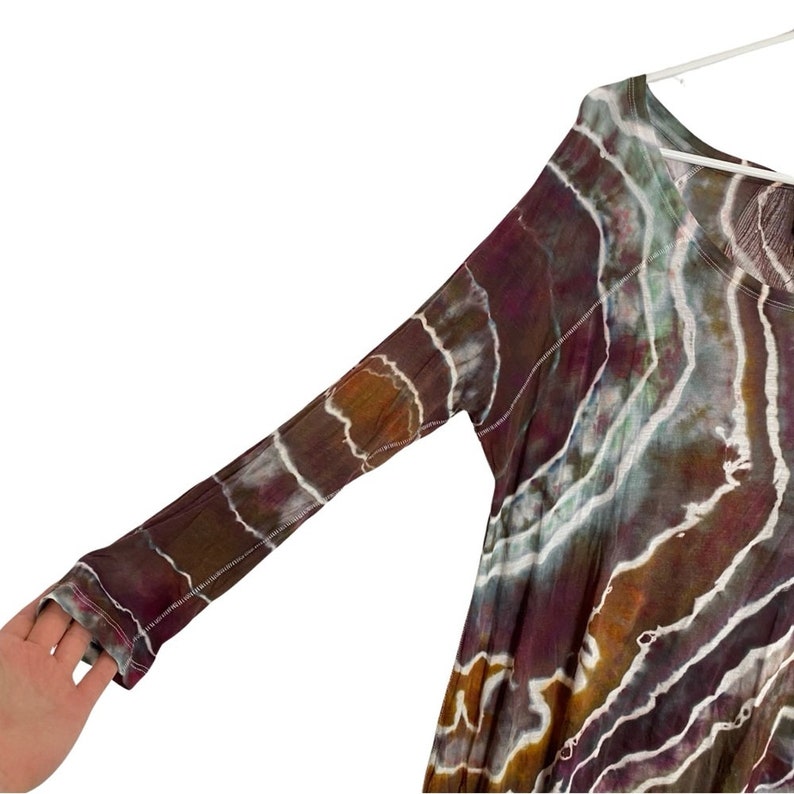 May include: A long-sleeved, tie-dye shirt with a brown, purple, and white color scheme. The shirt has a relaxed fit and a round neckline.