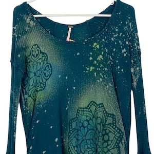 May include: Teal blue long-sleeved shirt with a white and green mandala pattern and a splatter paint design.