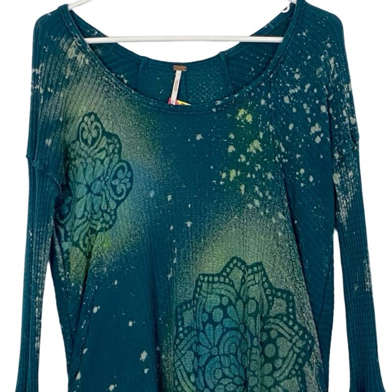 May include: Teal blue long-sleeved shirt with a white and green mandala pattern and a splatter paint design.