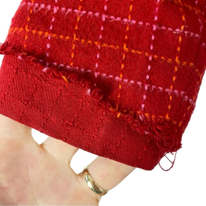 May include: Red fabric with a pink and orange plaid pattern. The fabric has a frayed edge.