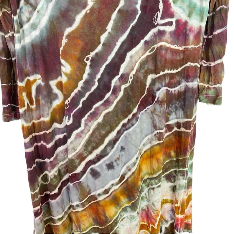 May include: A tie-dye shirt with a colorful, abstract pattern in shades of purple, brown, orange, and white. The shirt has a relaxed fit and a slightly longer length.