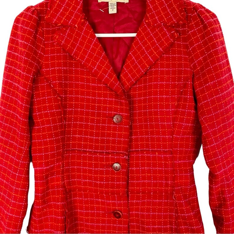 May include: Red blazer with a checkered pattern in pink and white. The blazer has a button closure and a collar.