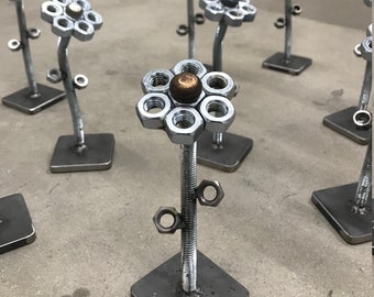 May include: A collection of metal flower sculptures made from nuts and bolts. Each flower has a different colored center bead.