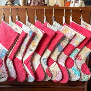 May include: A collection of ten Christmas stockings, each with a vibrant red body and a patchwork design on the cuff. The stockings are hung on a wooden cabinet with brass hooks, ready for the holiday season.