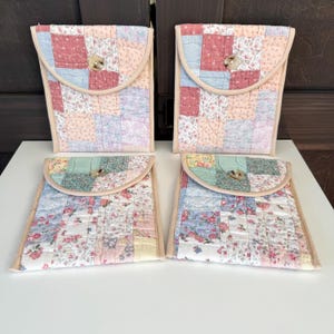 May include: Four quilted fabric pouches with patchwork designs. The pouches feature a variety of pastel colors, including pink, blue, and green, with floral patterns. Each pouch has a rounded flap secured with a wooden button and a beige trim.