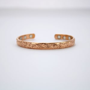 May include: A copper bracelet with a floral design and magnetic closures.