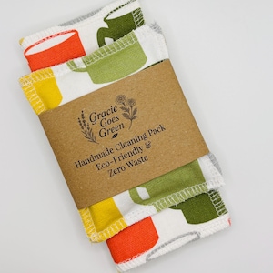 May include: A pack of handmade cleaning cloths, held together by a brown paper band. The cloths feature a white background with colorful cup designs in orange, yellow, and green. The band reads "Gracie Goes Green" and "Handmade Cleaning Pack Eco-Friendly & Zero Waste."