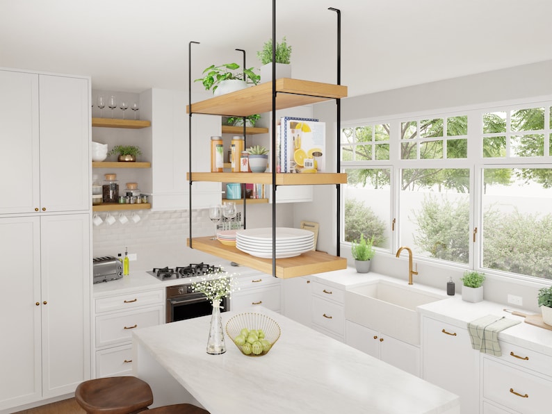 May include: A white kitchen with a floating shelf unit made of wood and black metal. The shelf unit is filled with various items, including plants, books, and dishes. The kitchen also features a white farmhouse sink, a white worktop, and white cabinets.