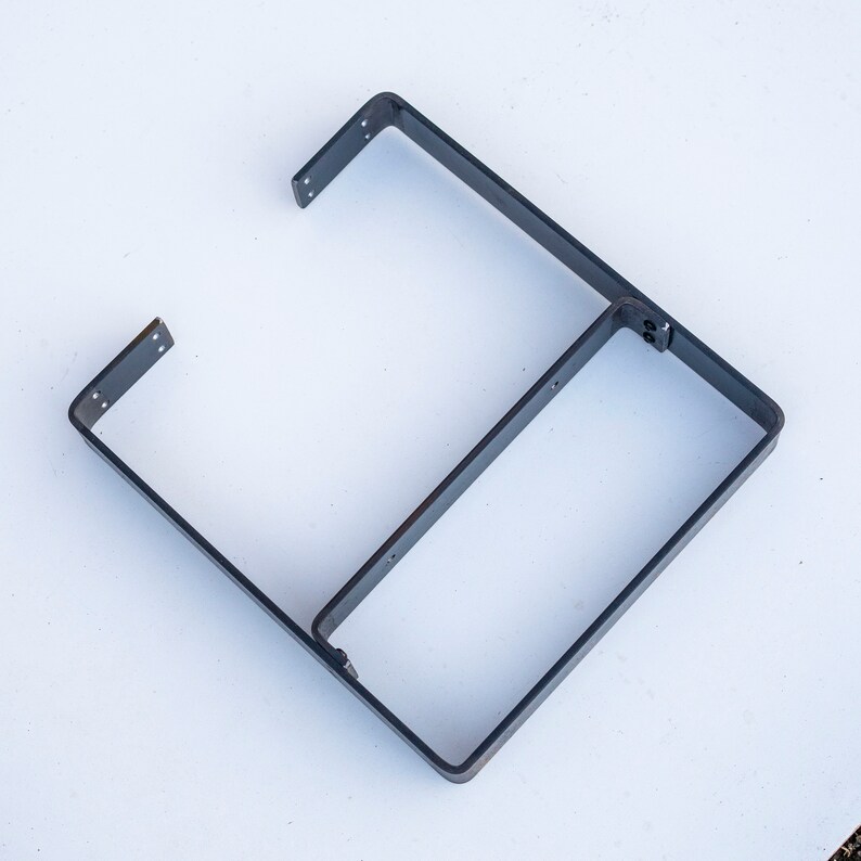 May include: A metal shelf bracket with two shelves. The bracket is made of black metal and has a simple, industrial design.