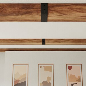 May include: Three framed abstract art prints with muted colours and geometric shapes hang on a white wall beneath a wooden beam ceiling.