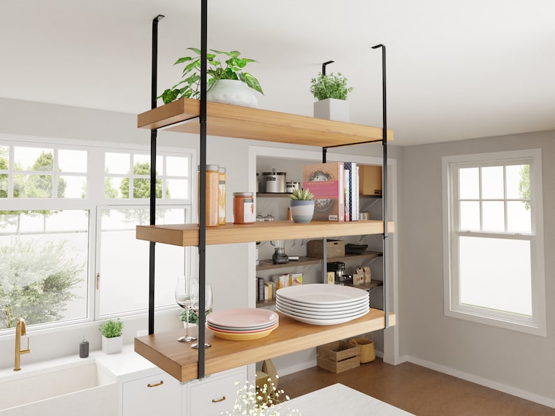 May include: Three wooden shelves with black metal supports are suspended from the ceiling. The shelves are filled with various items, including plants, books, dishes, and jars.