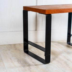 May include: A wooden table top with a black metal frame. The table has a simple design with a rectangular top and a square base.