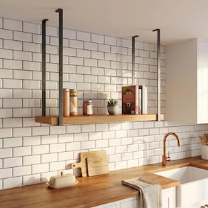 May include: A wooden floating shelf suspended from the ceiling by black metal supports. The shelf holds jars, a small potted plant, and books. The kitchen features white subway tile and a wooden countertop.