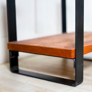 May include: A wooden shelf with a black metal frame. The shelf is made of natural wood and has a simple, modern design.