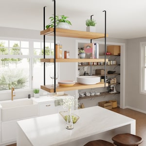 May include: A white kitchen island with a white worktop and a hanging wooden shelf unit with black metal supports. The shelf unit has three shelves and is filled with various items, including plants, dishes, and books. The kitchen island is also decorated with a vase of white flowers.
