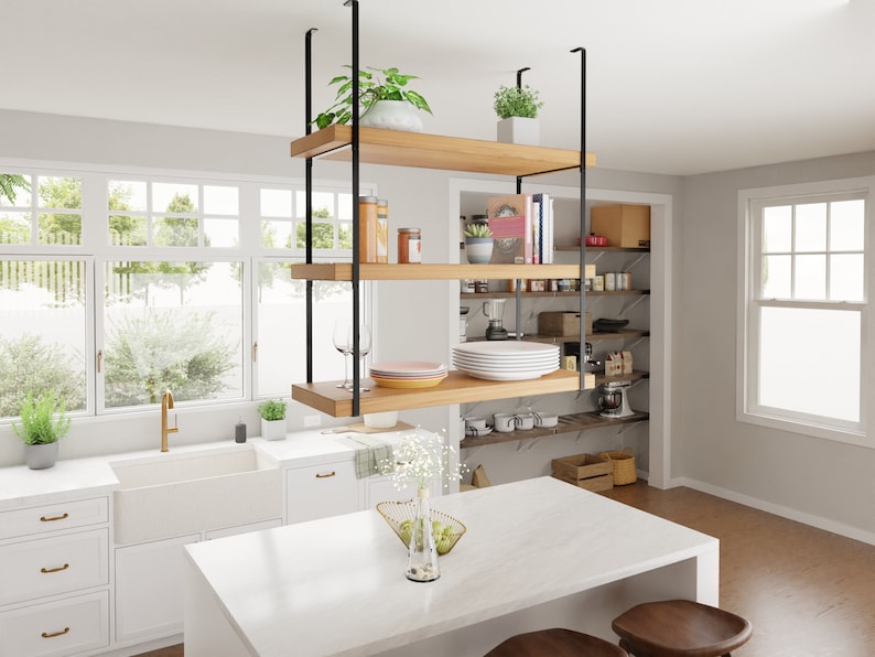 May include: A white kitchen island with a white worktop and a hanging wooden shelf unit with black metal supports. The shelf unit has three shelves and is filled with various items, including plants, dishes, and books. The kitchen island is also decorated with a vase of white flowers.