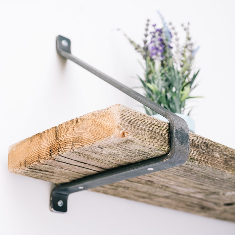 K&ouml;nnte beinhalten: Ein rustikales Holzregal mit Metallkonsolen. Das Regal ist aus wiederverwendetem Holz gefertigt und hat eine nat&uuml;rliche, verwitterte Oberfl&auml;che. Die Metallkonsolen sind schwarz und haben ein schlichtes, industrielles Design.