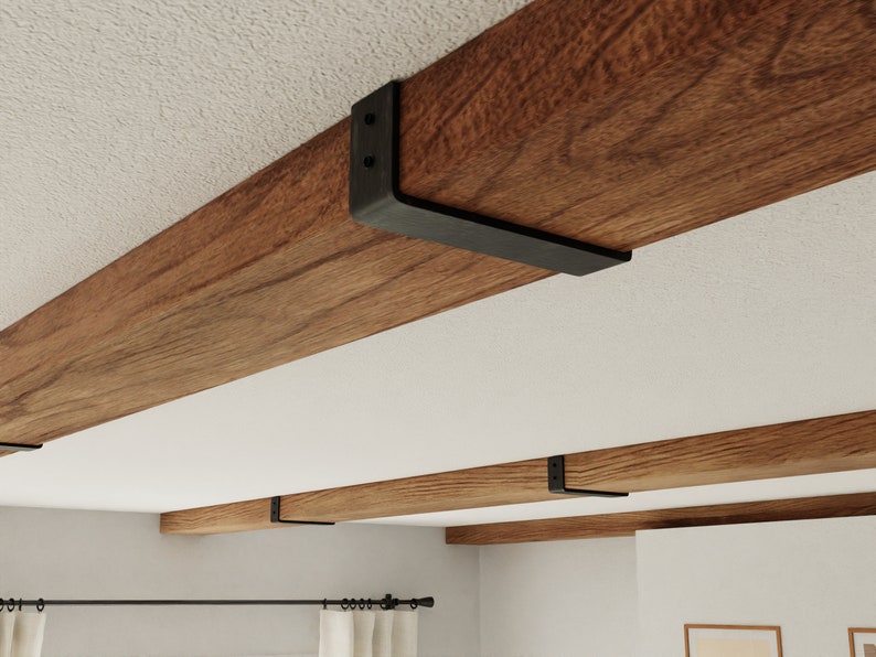 May include: A set of four black metal brackets supporting a wooden beam on a white ceiling. The brackets are L-shaped and have two holes on each side. The beam is made of dark wood with a natural grain.