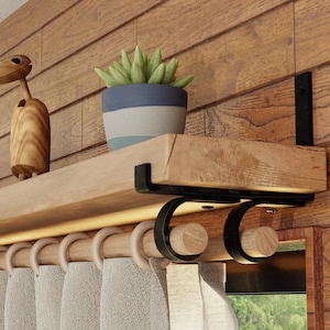 May include: A wooden shelf with black metal brackets is mounted on a wood wall. A small potted succulent plant sits on the shelf. A wooden curtain rod with rings is mounted below the shelf. White curtains hang from the rod.