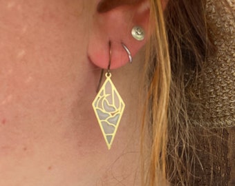 Könnte beinhalten: Goldene geometrische Ohrringe mit einem filigranen, komplizierten Design. Die Ohrringe sind diamantförmig und haben eine strukturierte Oberfläche.