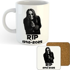 May include: White ceramic mug with a black and white image of a man in sunglasses, and the text "RIP 1948-2025". A square coaster with the same design is also present, alongside a cork coaster.