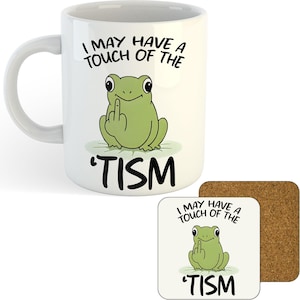 May include: White ceramic mug with a humorous design featuring a green frog giving the middle finger. The text reads "I MAY HAVE A TOUCH OF THE 'TISM". A matching coaster is also visible.