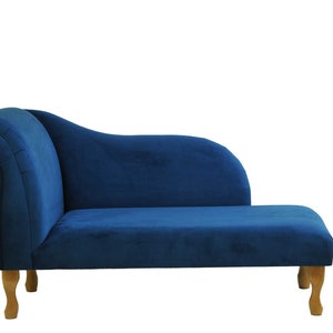 Puede incluir: Una chaise longue de terciopelo azul con patas de madera. La chaise longue tiene un respaldo curvo y un asiento acolchado.