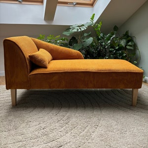 Op de afbeelding: Een chaise longue van mosterdgele corduroy met houten poten. De chaise longue staat op een lichtgrijs tapijt in een kamer met een dakraam.