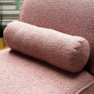 May include: A close-up of a pink textured armchair with a matching pink cylindrical pillow. The fabric has a soft, fuzzy texture.