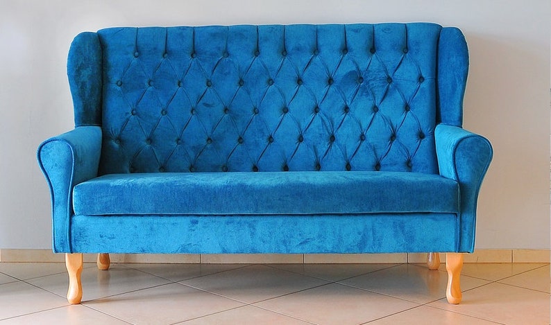 May include: A blue velvet tufted sofa with wooden legs. The sofa has a high back and wingback arms.