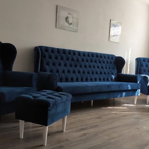 May include: A living room set with a blue velvet sofa, two armchairs, and a matching ottoman. The furniture has a tufted design and white legs.