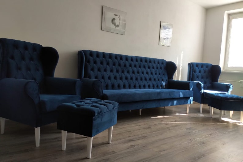 May include: A living room set with a blue velvet sofa, two armchairs, and a matching ottoman. The furniture has a tufted design and white legs.