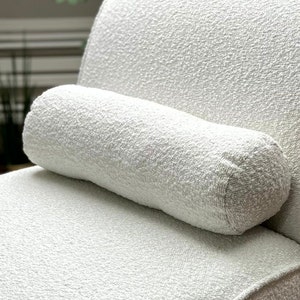 May include: A white, textured throw pillow with a cylindrical shape. The pillow is made of a soft, fluffy material.