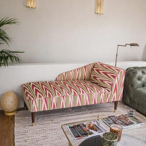Può includere: Una chaise longue rivestita in tessuto con un motivo ikat ripetuto nei toni del rosso, verde e crema. Il mobile è dotato di un unico bracciolo inclinato, una seduta imbottita e quattro gambe in legno affusolate con piedini in metallo dorato.