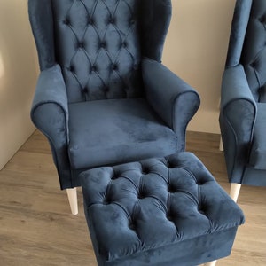 May include: A blue velvet wingback armchair with a tufted back and seat, and a matching blue velvet ottoman with white legs.