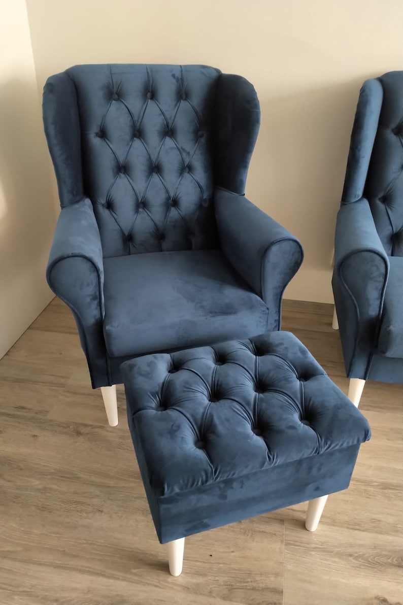 May include: A blue velvet wingback armchair with a tufted back and seat, and a matching blue velvet ottoman with white legs.