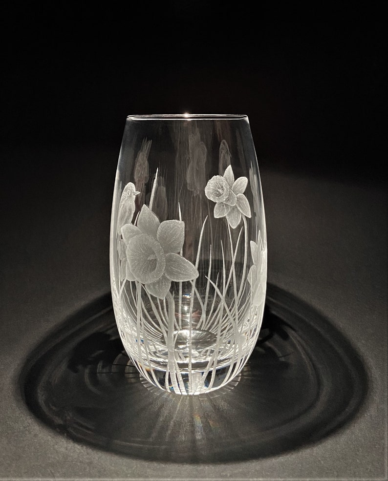 K&ouml;nnte beinhalten: Eine klare Glasvase mit einem ge&auml;tzten Design aus Narzissen und einem Vogel. Die Vase ist oval geformt und hat eine schmale &Ouml;ffnung.