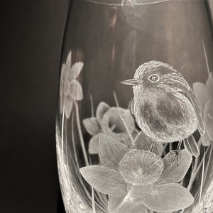K&ouml;nnte beinhalten: Eine klare Glasvase mit einem ge&auml;tzten Design eines Rotkehlchens, das auf einer Narzisse sitzt. Die Vase ist oval geformt und hat ein zartes, filigranes Design.