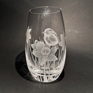 K&ouml;nnte beinhalten: Eine klare Glasvase mit einem ge&auml;tzten Design eines Rotkehlchens, das auf einer Narzissenbl&uuml;te sitzt. Die Vase hat einen abgerundeten Boden und eine schmale &Ouml;ffnung.