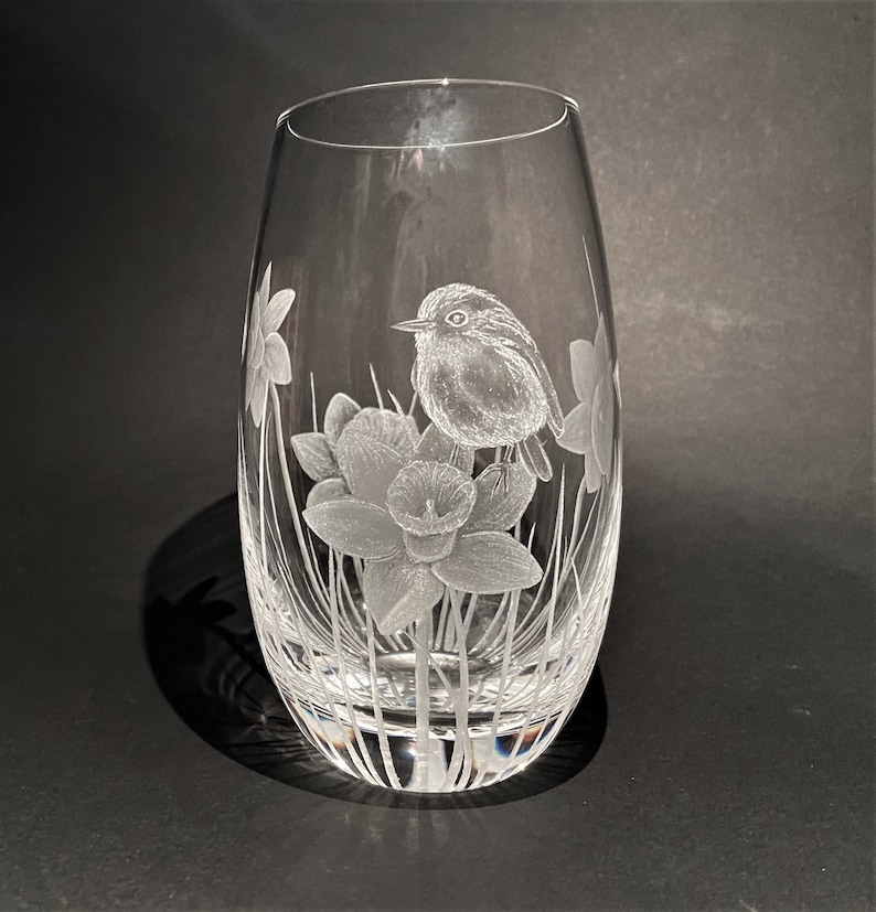 K&ouml;nnte beinhalten: Eine klare Glasvase mit einem ge&auml;tzten Design eines Rotkehlchens, das auf einer Narzissenbl&uuml;te sitzt. Die Vase hat einen abgerundeten Boden und eine schmale &Ouml;ffnung.