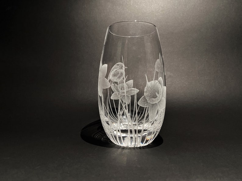 K&ouml;nnte beinhalten: Eine klare Glasvase mit einem ge&auml;tzten Design aus Narzissen und einem Rotkehlchen. Die Vase hat einen abgerundeten Boden und einen zylindrischen oberen Teil.