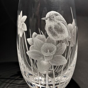 K&ouml;nnte beinhalten: Eine klare Glasvase mit einem ge&auml;tzten Design eines Rotkehlchens, das auf einer Narzisse sitzt. Die Vase hat einen runden K&ouml;rper und einen schmalen Hals.