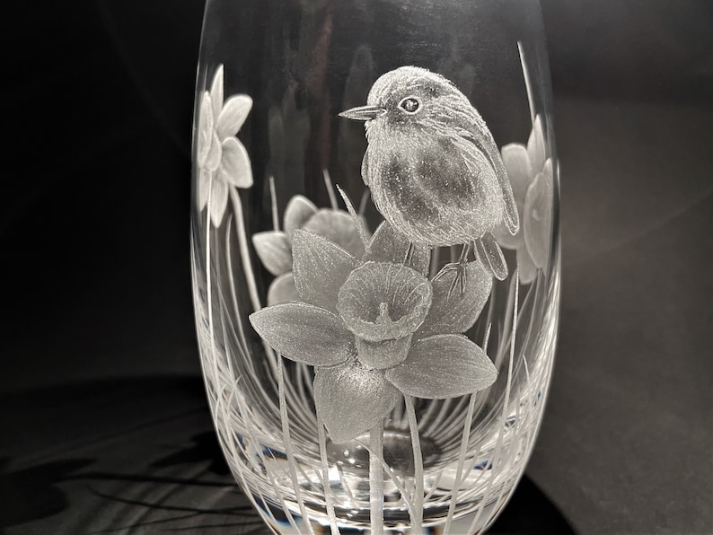 K&ouml;nnte beinhalten: Eine klare Glasvase mit einem ge&auml;tzten Design eines Rotkehlchens, das auf einer Narzisse sitzt. Die Vase hat einen runden K&ouml;rper und einen schmalen Hals.
