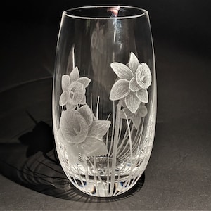 K&ouml;nnte beinhalten: Eine klare Glasvase mit einem ge&auml;tzten Design von Narzissen. Die Vase hat einen runden Boden und eine hohe, schlanke Form.