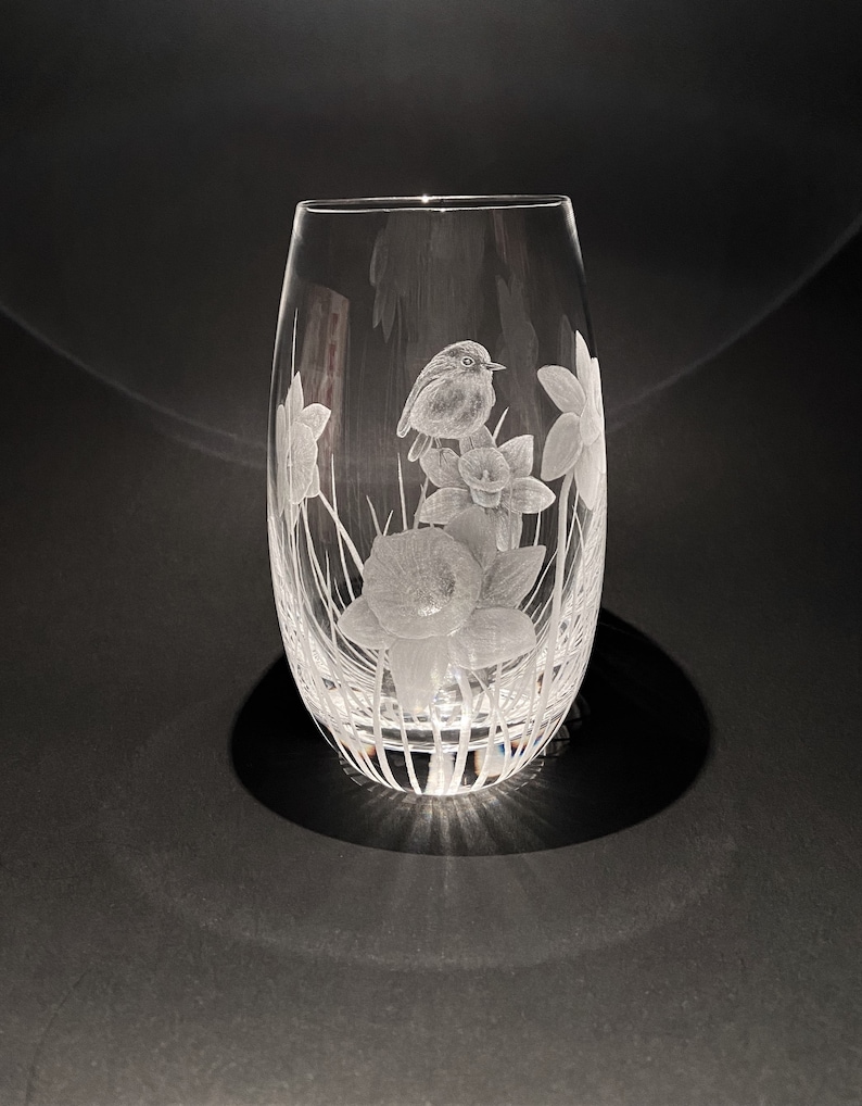 K&ouml;nnte beinhalten: Eine klare Glasvase mit einem ge&auml;tzten Design eines Rotkehlchens, das auf einer Gruppe von Narzissen sitzt.