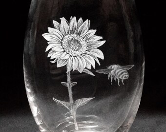 May include: A clear glass vase with an etched design of a sunflower and a bee. The vase is oval shaped and has a wide mouth.