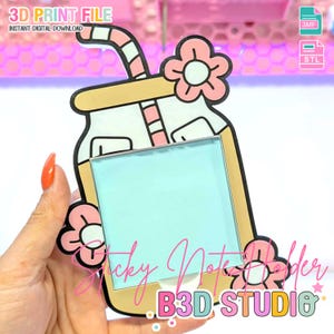 May include: A decorative sticky note holder shaped like a drink, featuring a light blue note area. The holder has a black and beige outline, pink flower details, and a striped straw. Text on the holder reads "Sticky Note Holder" and "B3D-STUDIO".