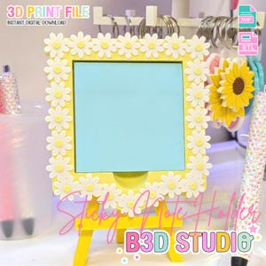 Puede incluir: Un soporte para notas adhesivas amarillo con un marco de flores de margarita y una nota azul claro. El soporte tiene un pequeño caballete. El texto de la imagen incluye "3D PRINT FILE", "INSTANT DIGITAL DOWNLOAD", "Sticky Note Holder" y "B3D STUDIO".