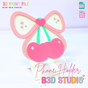 Può includere: Un supporto per telefono a forma di ciliegia rosa e verde con un design a fiocco. Il supporto per telefono riporta le parole "Phone Holder" e "B3D STUDIO" in un carattere corsivo. L'immagine include anche il testo "3D PRINT FILE" e "INSTANT DIGITAL DOWNLOAD".